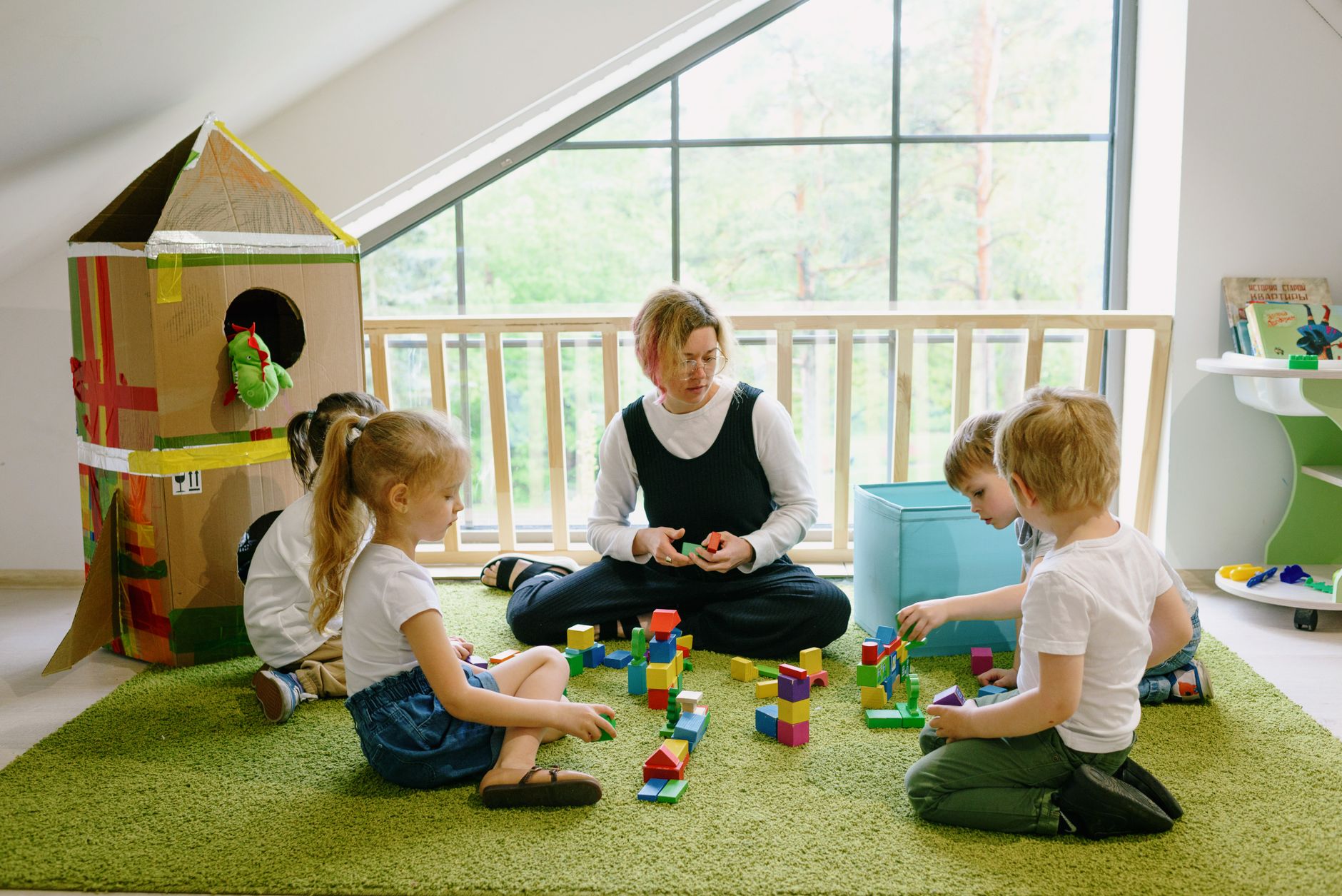 Children playing with building blocks and a cardboard house in a cozy classroom